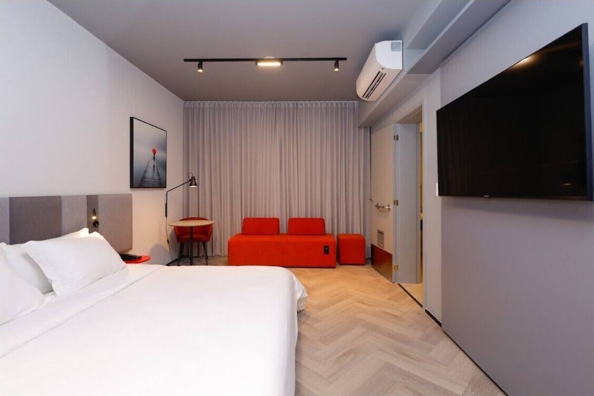 A modern hotel room with a bed, a red sofa, a small table, and a TV.