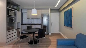 A modern kitchen with built-in appliances, a dining area with a round table and chairs, and a blue sofa in the living area. - Urban Home Stay - Santa Maria (Recife)