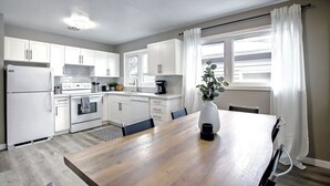 Et moderne køkken med hvide skabe, et træspisebord og et vindue med gardiner.