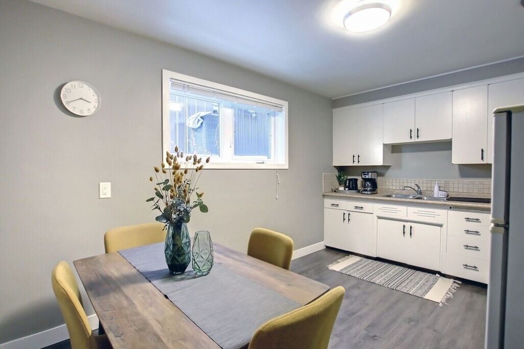 Una cocina moderna con armarios blancos, una mesa de comedor con sillas, un reloj en la pared y una ventana con persianas.