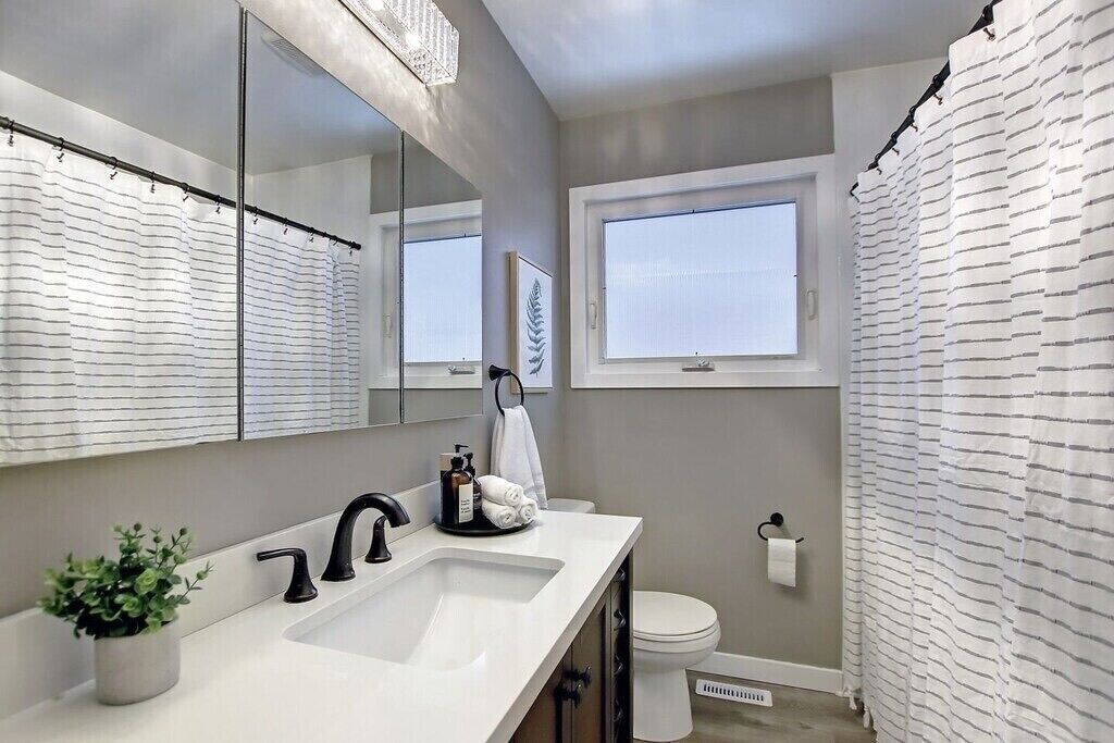 A modern bathroom with a large mirror, a white sink, a toilet, and a shower curtain.
