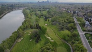 Oversigtsbillede af en golfbane med en flod på den ene side og en bysilhouet i det fjerne.