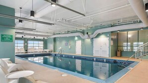 Ein Schwimmbecken mit gefliestem Rand, eine Decke mit freiliegenden Rohren und ein Schild, das Freizeiteinrichtungen anzeigt.