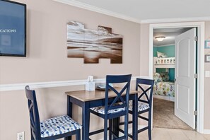 Ein Essbereich mit einem Holztisch, vier Stühlen, einem an der Wand hängenden abstrakten Gemälde und einer teilweise sichtbaren Tür zu einem Kinderzimmer.