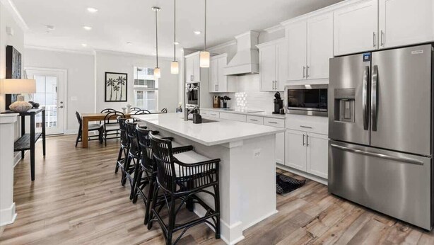 Una cocina moderna con armarios blancos, un refrigerador de acero inoxidable y una isla central con taburetes de bar.