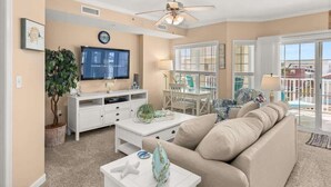 A living room with a beige sofa, a white coffee table, a television, and a ceiling fan. - Seaside Escape Mansion (Ocean City)