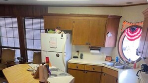 Eine kleine Küche mit Holzschränken, einem Kühlschrank, einer Spüle und einem Essbereich mit Tisch und Stühlen.