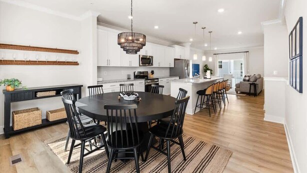 A modern kitchen with white cabinets, a central island, and a dining area with a round table and chairs.