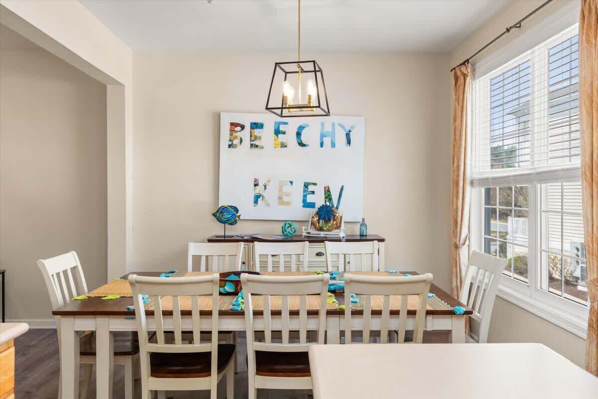 Un coin repas avec une table et des chaises blanches, un luminaire suspendu et un mur orné d’une enseigne color ée.