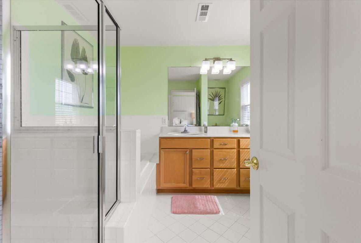 A bathroom with a glass shower enclosure, a wooden vanity with a mirror, and a white sink.