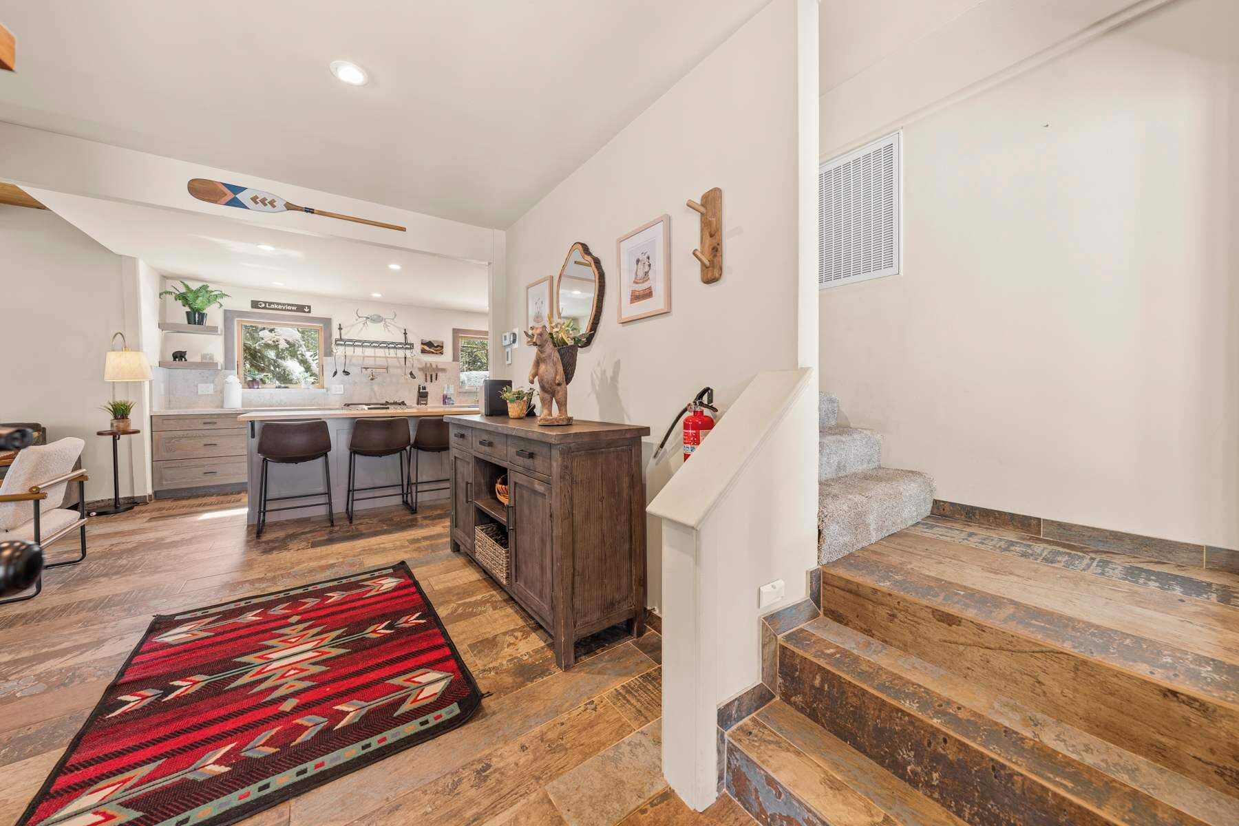 Una cocina moderna con taburetes de bar, una escalera de madera y un tapete rojo estampado.