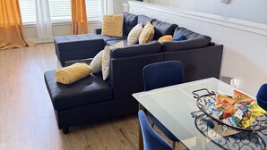Una sala moderna con un sofá modular, una mesa de comedor de cristal y sillas azules.