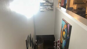 Una escalera con barandilla, una pared con cuadros enmarcados y un cuadro abstracto colorido.
