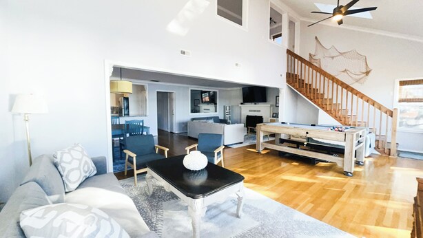A spacious living room with a pool table, a sofa, and a dining table. A staircase with a wooden railing leads to an upper level.