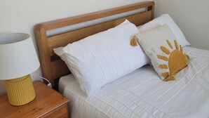 A bed with white bedding, a wooden headboard, a lamp on a wooden nightstand, and a pillow with a paw print design.