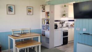 A compact kitchen with a dining area, a clock, and framed pictures on the wall.