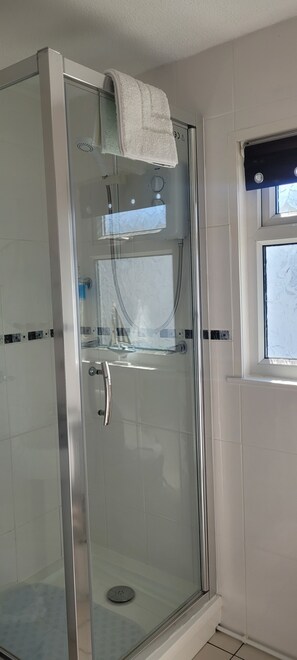 Eine Dusche mit Glasabtrennung, an der ein weißes Handtuch an der Tür hängt.
