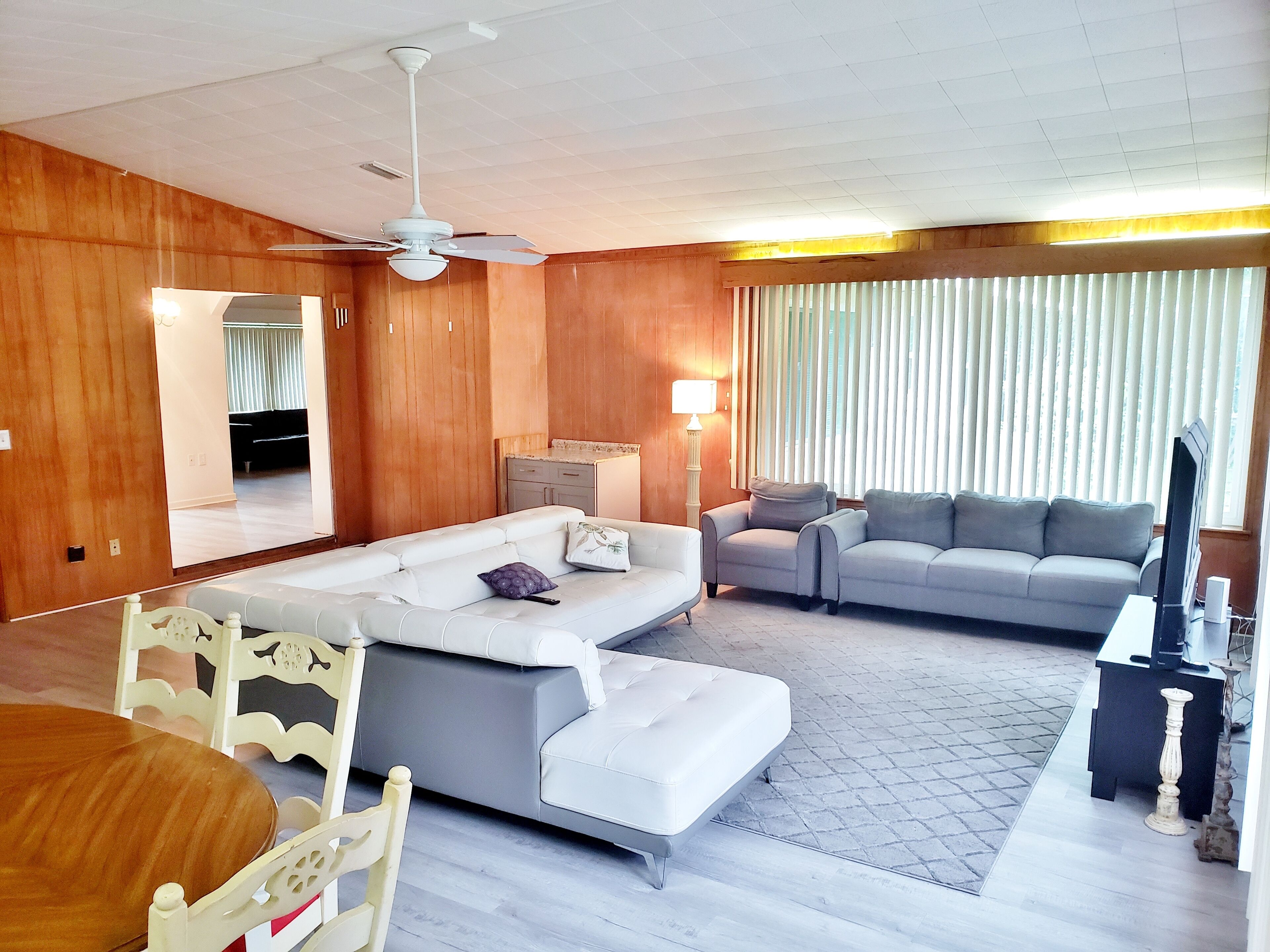 Una sala de estar con sofá, una mesa de comedor con sillas, un televisor y un ventilador de techo.