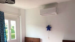 A bedroom with two single beds, a window with curtains, an air conditioning unit, and a star-shaped decoration on the wall.