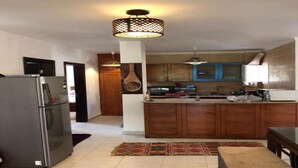 A modern kitchen with a central island, wooden cabinets, and a stainless steel refrigerator.
