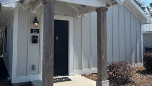 Un bâtiment blanc avec une porte noire, un panneau indiquant le numéro « 123 », et un porche doté de piliers en bois.