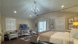 Une chambre spacieuse avec un grand lit, une télévision, un lustre et une vue sur l’extérieur par la fenêtre.