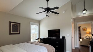 Een slaapkamer met een bed, een televisie, een plafondventilator, een dressoir en een raam met jaloezieën.