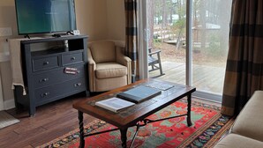 Een woonkamer met een televisie, een bank, een fauteuil, een salontafel en uitzicht op de omgeving.