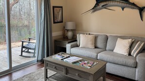 Un salon avec un canapé gris, une table basse sur laquelle sont posés des magazines, une lampe et un grand poisson décoratif accroché au mur.