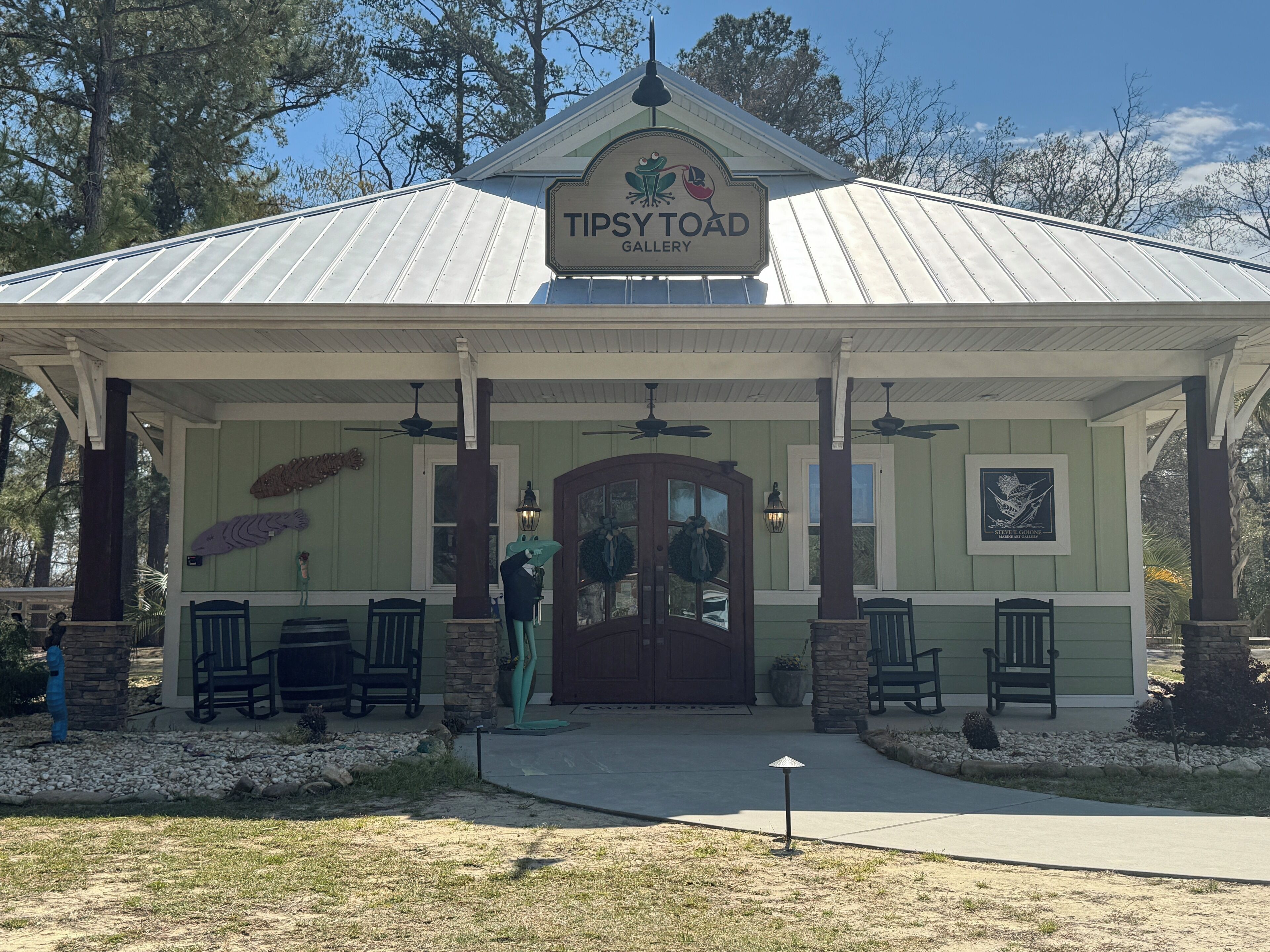 A building with a sign reading "Tipsy Toad Gallery" and a covered entrance with benches and a decorative wall.