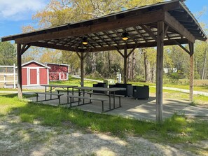 A covered picnic area with tables and benches, a red building, and a grassy field. - Luxury Lodging, Lakefront View ,King Bed w/Private Bath, Private Patio. (Elizabethtown)
