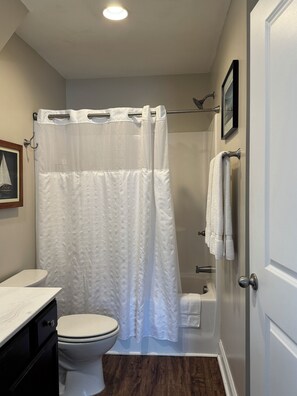 Ein Badezimmer mit weißem Duschvorhang, Toilette, Badewanne und Waschbecken mit weißer Arbeitsplatte.