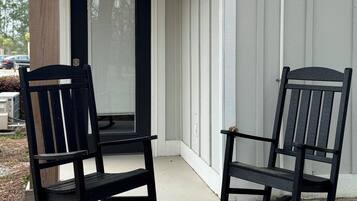 Two rocking chairs outside a building with a white exterior and a black door.