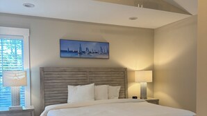 Une chambre avec un lit en bois, un ventilateur de plafond, un climatiseur, une table de chevet avec une lampe et une fenêtre avec des stores.