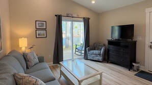 Un salon comprenant un canapé, une table basse avec un plateau en verre, un téléviseur posé sur un meuble et un ventilateur de plafond.