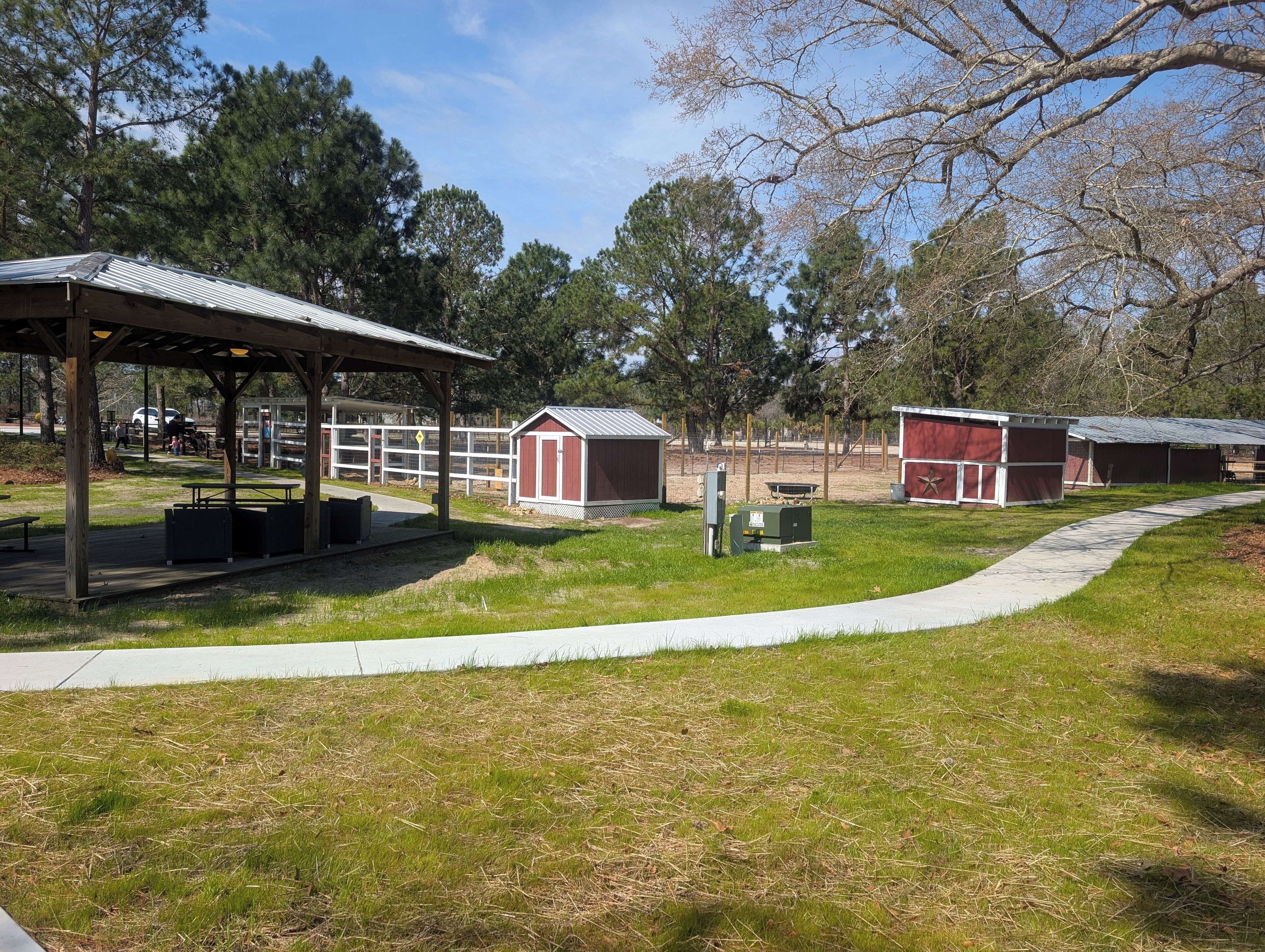 A park with a covered picnic area, red sheds, and a fenced playground.