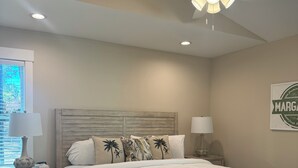 Une chambre à coucher avec un lit en bois, deux tables de chevet, un ventilateur de plafond et un appareil de climatisation.