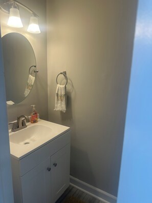 Ein Badezimmer mit einem weißen Waschbecken, einem Spiegel, einem Handtuchhalter und einer Seifenflasche.