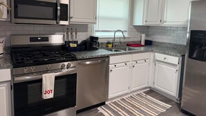 Une cuisine moderne avec des meubles blancs, un réfrigérateur en acier inoxydable, un four encastré, un four à micro-ondes et une cuisinière à gaz.