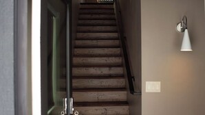 Eine Treppe mit Holzstufen führt zu einer oberen Etage, eine Glastür ist links und eine Wandleuchte rechts angebracht.