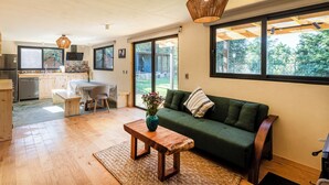 A modern kitchen with wooden cabinets, a dining table, and a sofa in a bright living area with large windows. - Villa Ahó (Valle de Bravo)