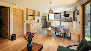 A modern kitchen with wooden cabinetry, a dining area with a table and chairs, and a large window offering a view of the outdoors. - Villa Ahó (Valle de Bravo)