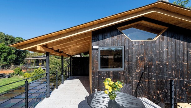 A modern wooden cabin with a covered porch, a large window, and a small garden area. - Villa Ahó (Valle de Bravo)