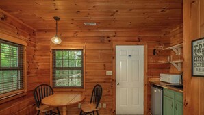 L’intérieur d’un chalet en bois comprend une table et des chaises, une porte blanche et un coin cuisine équipé d’un four à micro-ondes et d’un réfrigérateur.