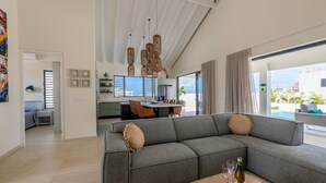 A modern living room with a gray sectional sofa, dining area, and large windows offering a view of the ocean.