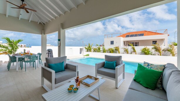 A rooftop pool area with outdoor seating, a table with drinks, and a view of a modern building.