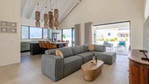 A modern living room with a grey sectional sofa, a wooden coffee table, and a dining area with chairs and a table.