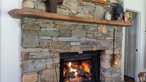Una chimenea de piedra con repisa de madera, un cuadro enmarcado de pájaros y un cubo de cobre.