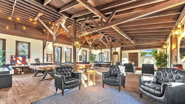 A spacious indoor area with a high ceiling, wooden beams, and a pool table. There are several black leather chairs and a blue patterned rug. - Tranquil Retreat W/hot-tub 10-mins to Downtown! (Fredericksburg)