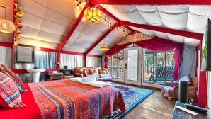 A spacious bedroom with a large bed, a sitting area with a sofa, and a view of the outdoors through a sliding door.